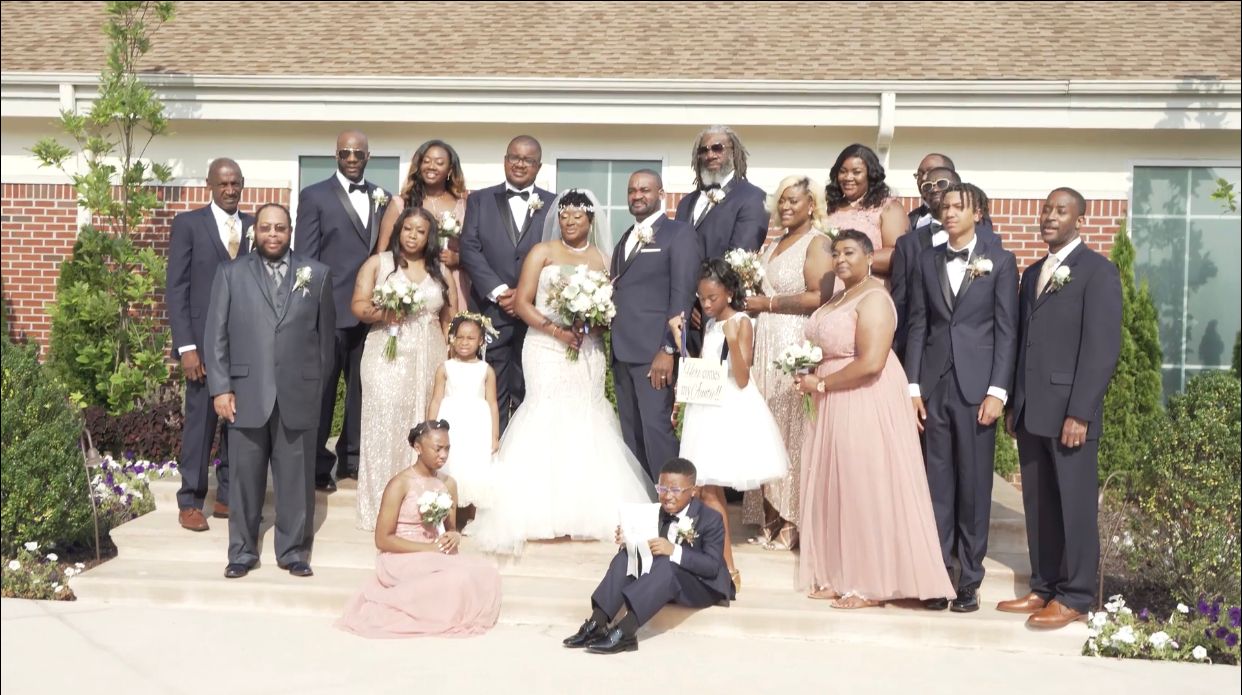 Large wedding party posing together outdoors in formal attire for a group photo.