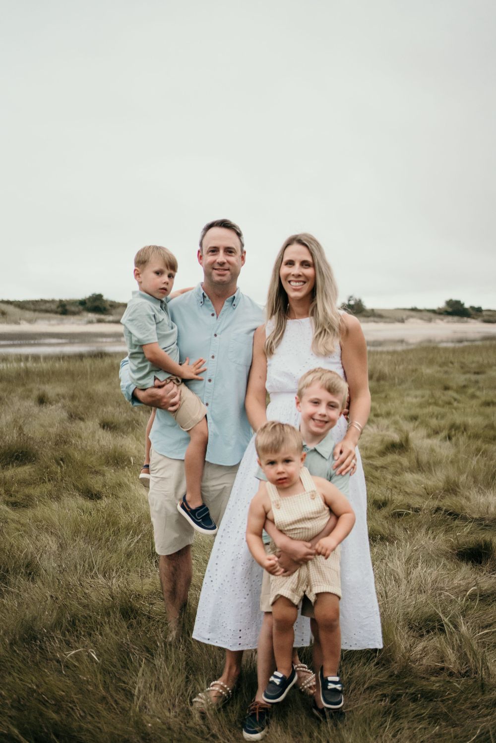Family portrait in casual coastal attire against overcast sky.