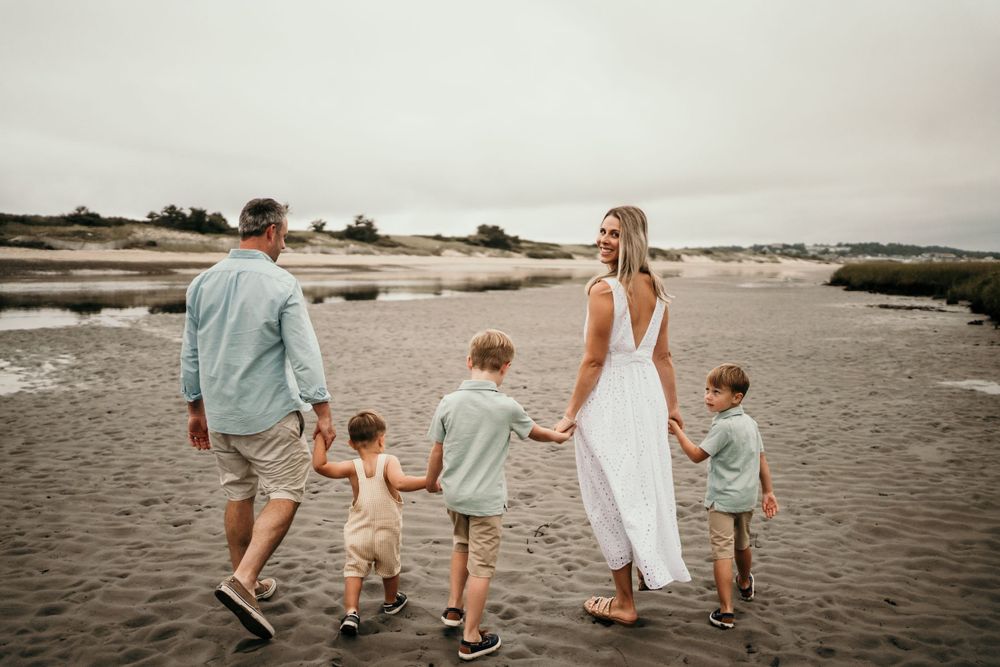 Family walking together on beach holding hands at sunset.
