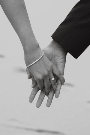 Close-up black and white photo of bride and groom holding hands, bride wearing a diamond ring and bracelet.