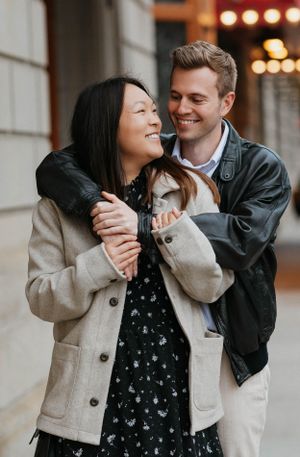 Happy engaged couple embracing and laughing together on a city street in autumn jackets.