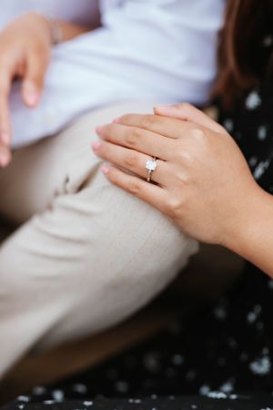 Close-up of an engagement ring with a solitaire diamond on a woman's hand resting on her knee.
