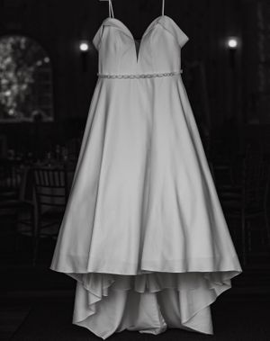 Elegant strapless white ball gown wedding dress with crystal belt hanging in black and white photo.