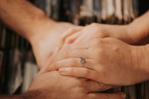 Close-up of elegant diamond engagement ring on woman's hand held by partner indoors.