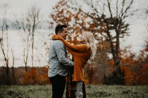 Couple embracing warmly outdoors with woman in burnt orange sweater among autumn trees.