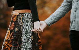 Close-up of couple holding hands showcasing woman's patterned boho skirt in fall outdoor setting.