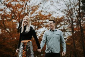 Happy couple holding hands and laughing while walking among vibrant red autumn foliage.