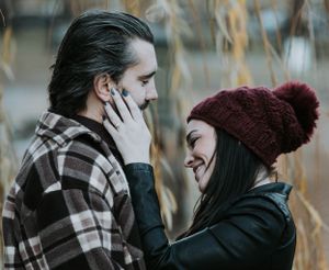 Couple sharing a tender moment outdoors in autumn, woman in red knit hat touching mans face.