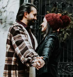 Happy couple holding hands and laughing together, woman wearing red beanie and leather jacket.