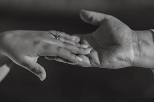 Black and white photo of two hands gently touching, one wearing an engagement ring.