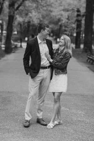 Black and white photo of a laughing couple walking together along a tree-lined park path.