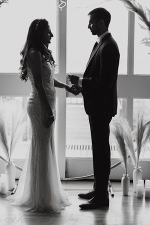 Silhouette of bride and groom holding hands during wedding ceremony with candles and pampas grass decor.
