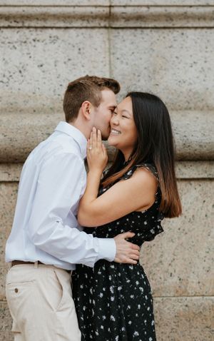 Man whispering in smiling woman's ear during romantic outdoor engagement photo session.