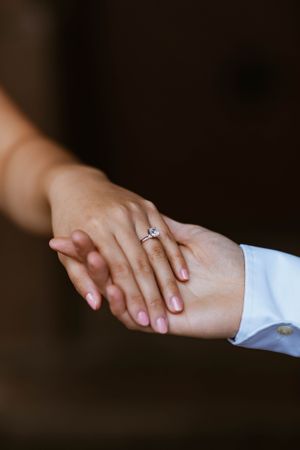Close-up of couple holding hands displaying a beautiful solitaire diamond engagement ring.