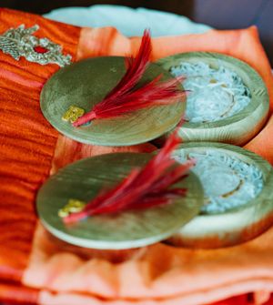 Decorative green cymbals with red feathers on orange silk fabric at wedding ceremony.