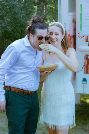 Bride and groom sharing food together laughing in front of colorful food truck.