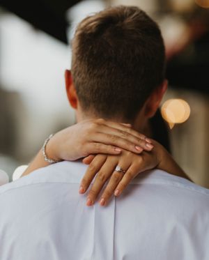 Close-up of womans hand with diamond engagement ring resting on mans shoulder during couples photo.