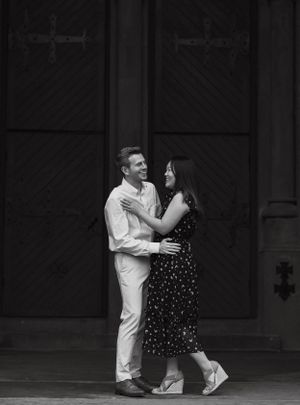 Black and white photo of couple slow dancing and gazing at each other in front of ornate wooden doors.