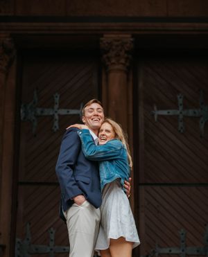 Joyful couple hugging and laughing in front of ornate wooden doors during an engagement photo session.