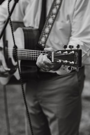Black and white close-up of musician playing acoustic guitar in white shirt.