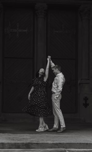 Black and white photo of couple dancing joyfully in front of ornate wooden doors during engagement session.