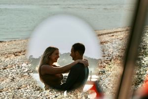 Romantic couple sitting together on a pebble beach, viewed through a circular reflection.