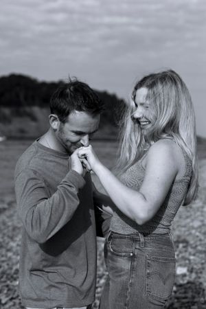 Man kissing womans hand as she laughs on a rocky beach in black and white.