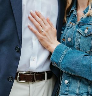 Close-up of a woman's hand with engagement ring resting on her partner's navy blazer.