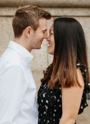 Romantic close-up of an engaged couple smiling and touching foreheads against a stone wall.