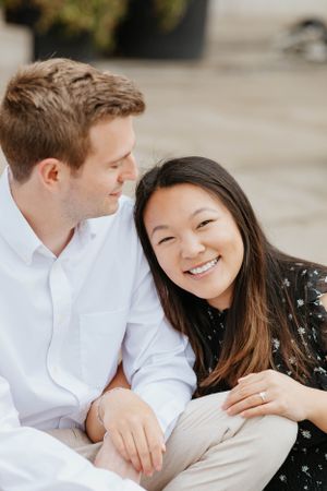 Happy engaged couple sitting together outdoors, woman smiling brightly wearing a floral black dress.