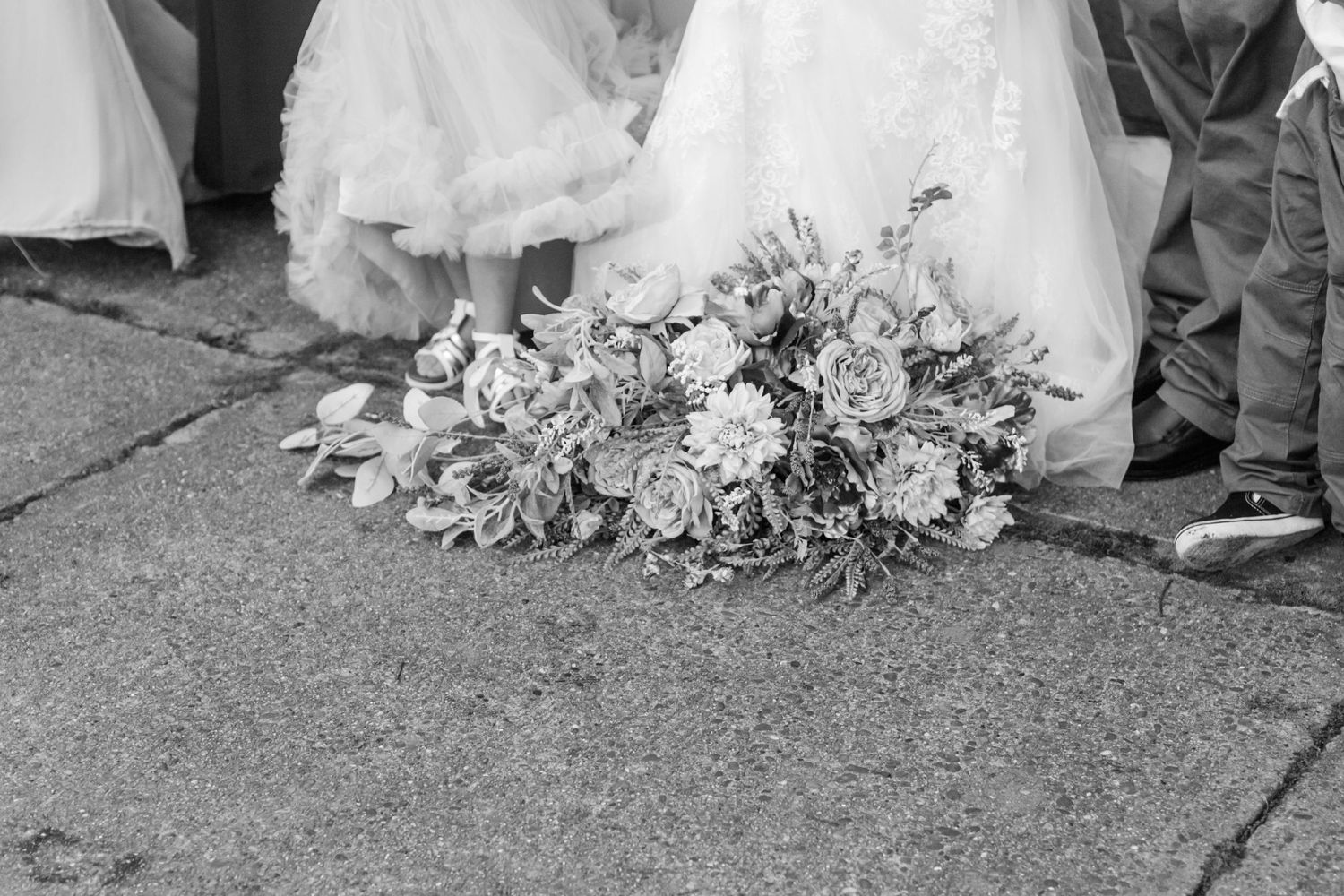 Black and white photo showing the bottom of wedding dresses and formal wear at a ceremony.