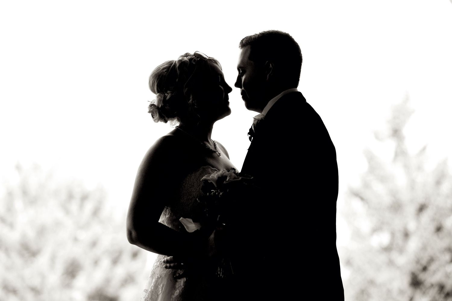 A romantic silhouette captures an intimate moment between newlyweds in black and white.