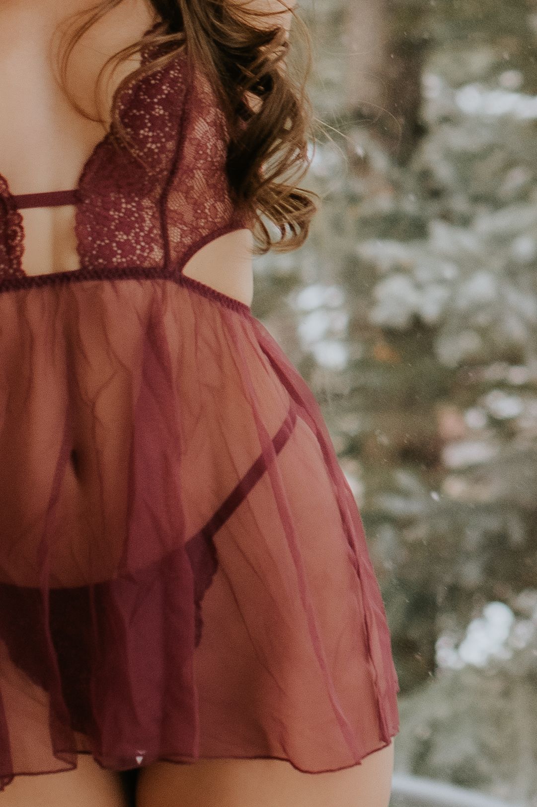 Close-up detail of a burgundy tulle dress with delicate layers and feminine styling against a soft blurred background.