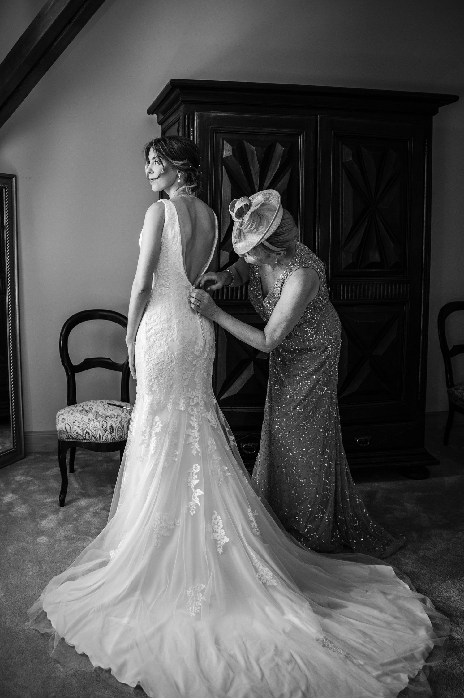 Black and white photo of a bride in lace gown getting final dress adjustments.