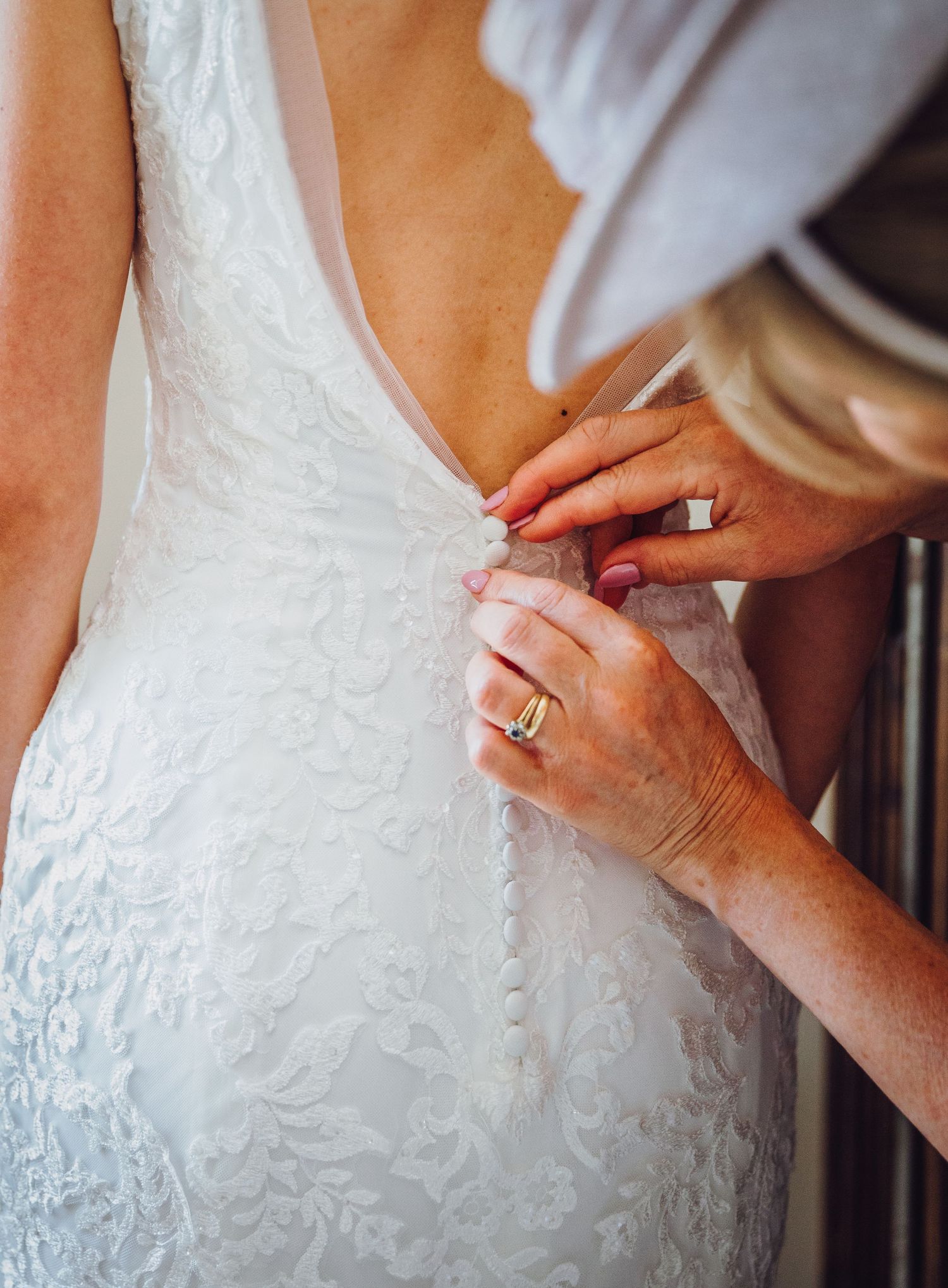 Close-up of hands adjusting the back of an ornate white lace wedding dress.