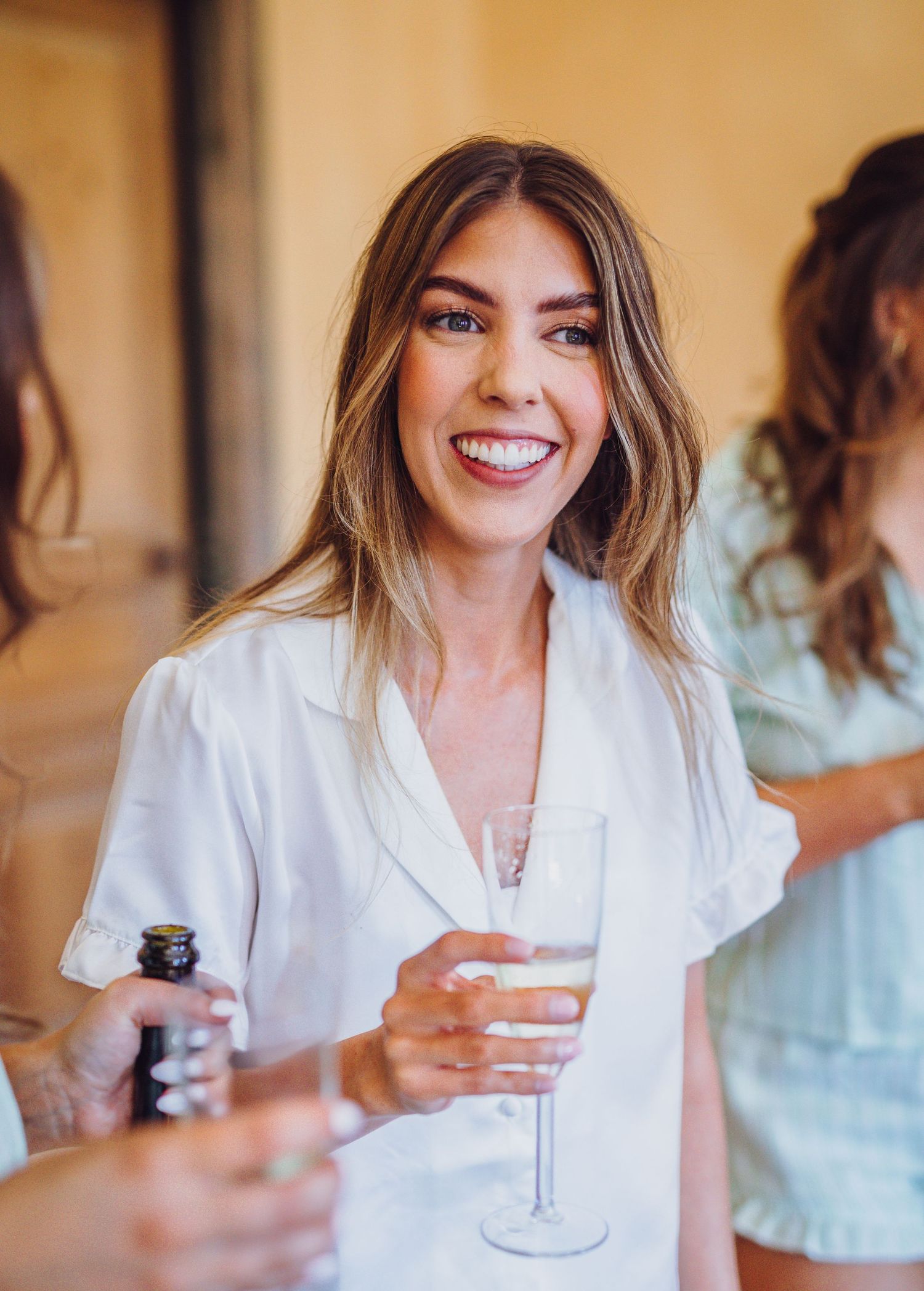 A person in a white outfit holding a drink and smiling warmly.