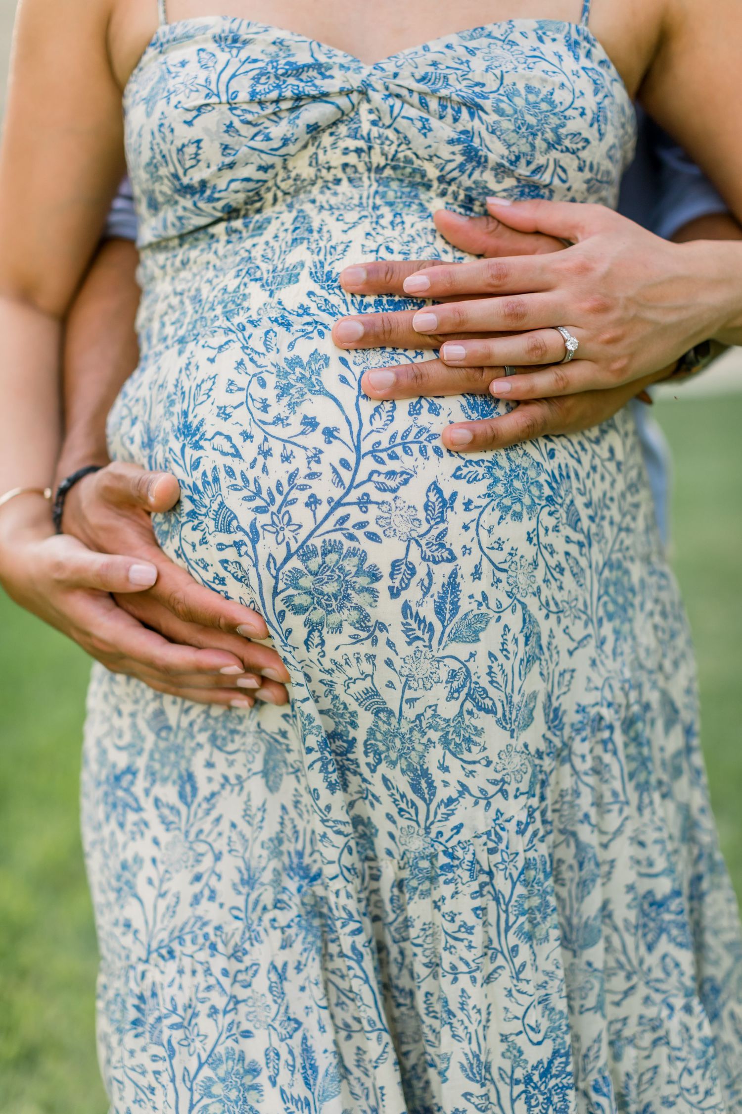 Close up of hands cradling baby bump in blue floral maternity dress.