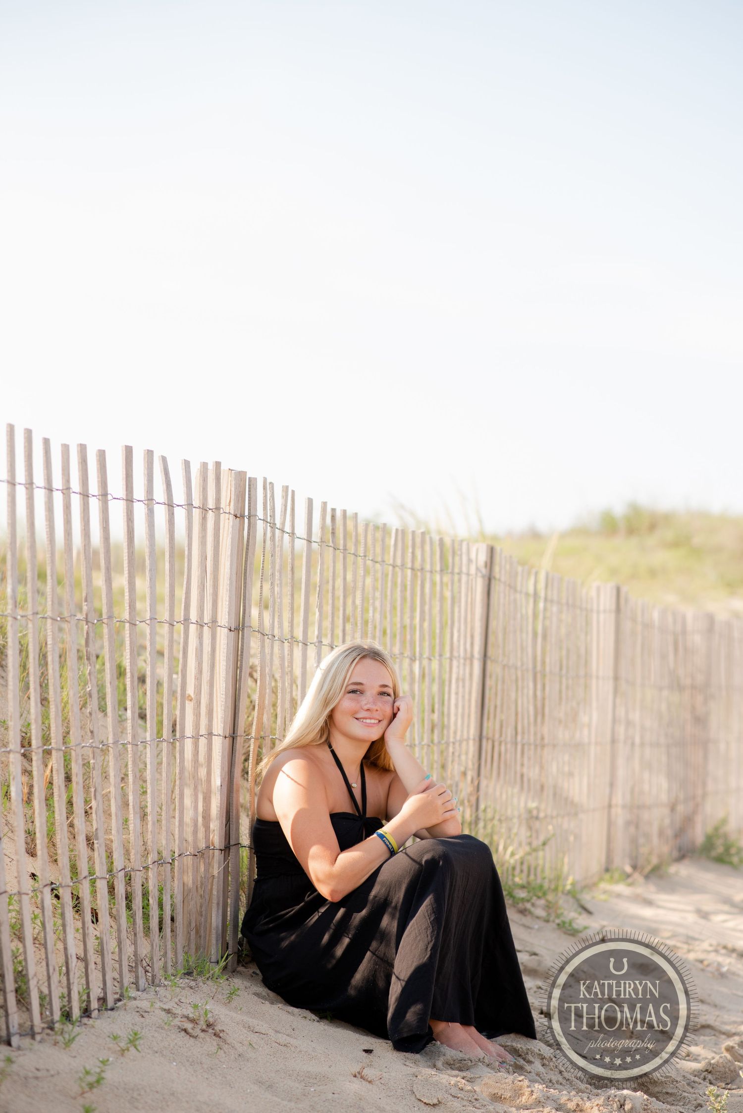 Beachside portrait next to sand fencing during sunset wearing black dress.