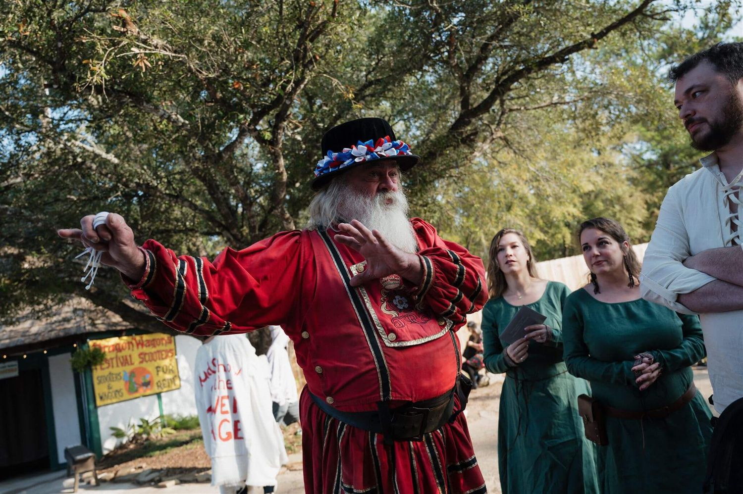 A performer in medieval red costume gestures while entertaining guests outdoors.