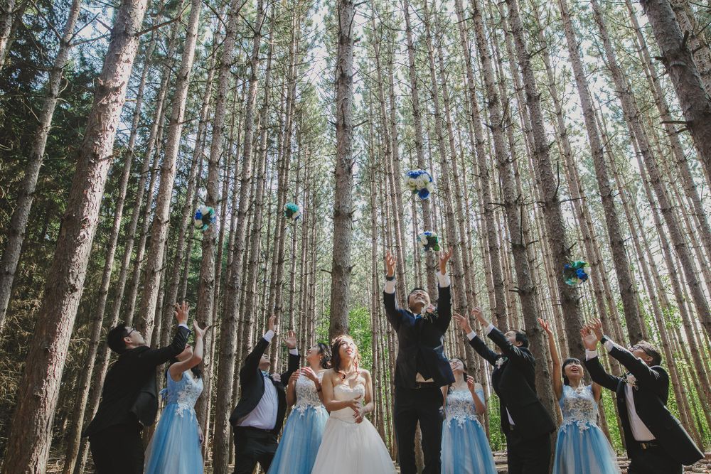 Wedding party celebrating with arms raised in tall pine forest.