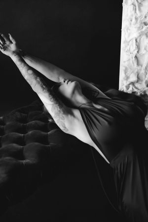 A graceful black and white artistic boudoir portrait of a woman stretching dramatically on a textured bench.