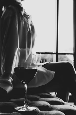 A glass of red wine sits on a soft surface near a woman in black and white monochromatic style boudoir photo.