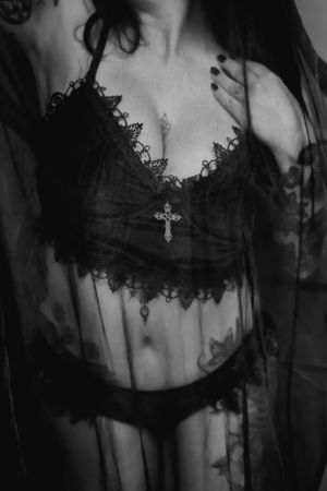 Black and white photo of woman in lingerie with lace trim and cross necklace detail against sheer fabric.