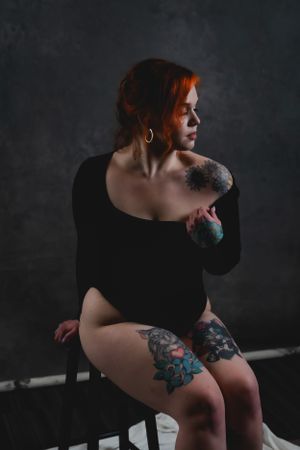 Artistic portrait of a person in black bodysuit with vibrant leg tattoos sitting on dark backdrop in Las Vegas.