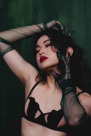 Artistic boudoir portrait against dark green background with black lace lingerie and sheer gloves.
