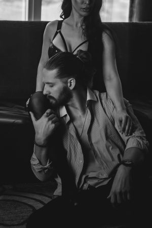 Artistic black and white photo of an intimate couple lounging together on a sofa in moody lighting.