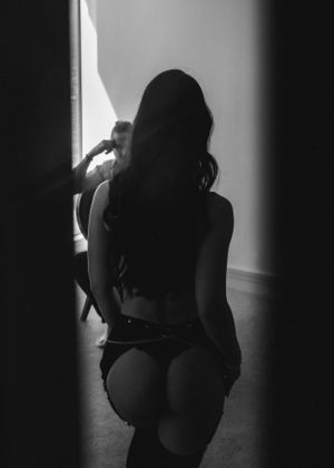 Black and white couple's boudoir image of a woman's silhouette in lingerie facing her partner with dramatic lighting.