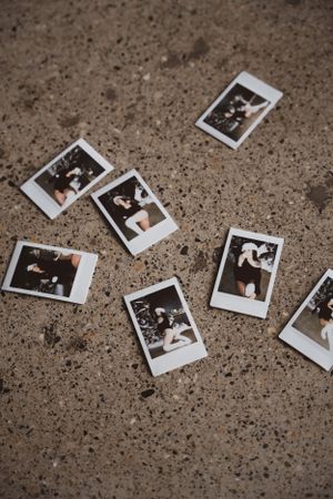 Several vintage-style boudoir Polaroid instant photos scattered on a textured concrete or stone surface in black and white tones.