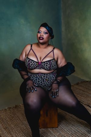 Studio portrait in moody lighting showing a curvy model in leopard print lingerie posing on a wooden box.