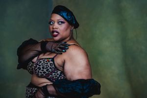 Artistic boudoir portrait of a plus-sized woman in leopard print lingerie and black sheer gloves against green background in Las Vegas.